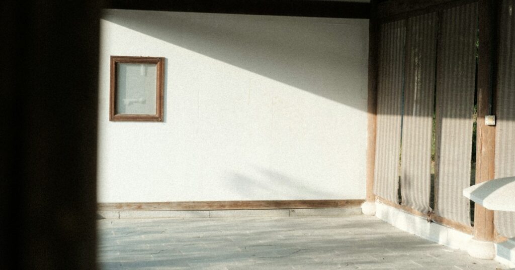 Morning sunlight falling across a plain white wall and a wooden floor in a quiet empty room