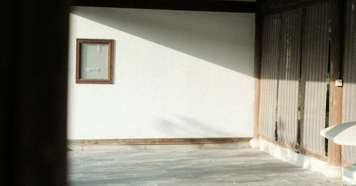 Morning sunlight falling across a plain white wall and a wooden floor in a quiet empty room