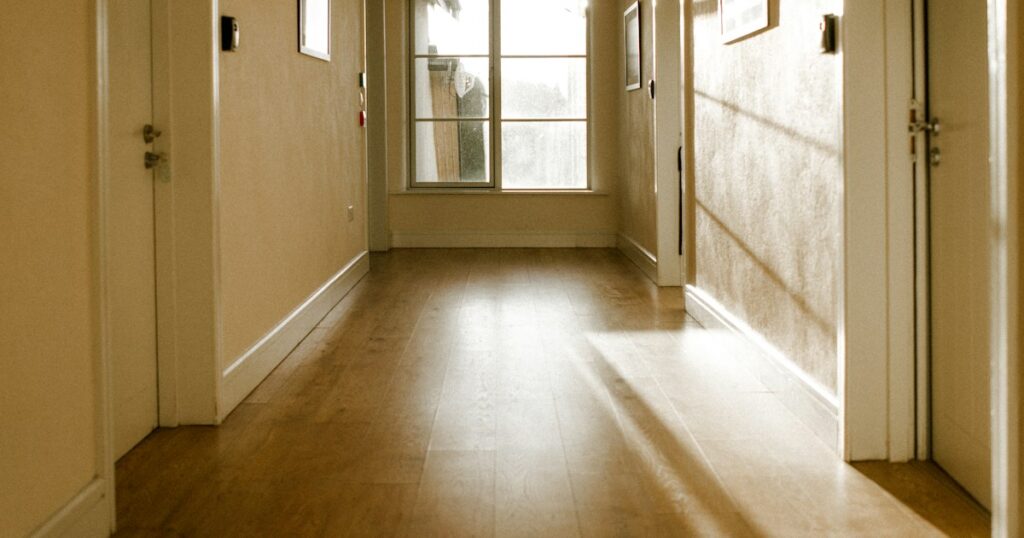 A quiet cream hallway with a wooden floor and daylight coming from a window at the far end