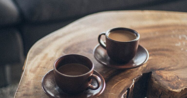 Two brown ceramic cups on a round wooden table in warm light