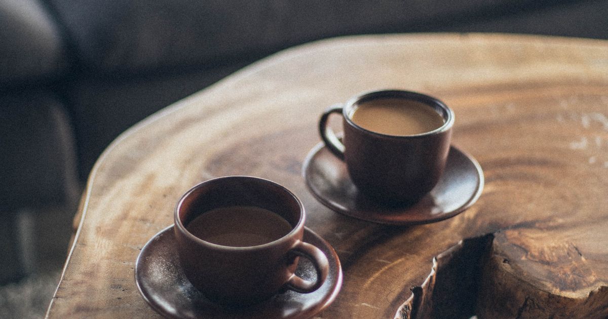 Two brown ceramic cups on a round wooden table in warm light