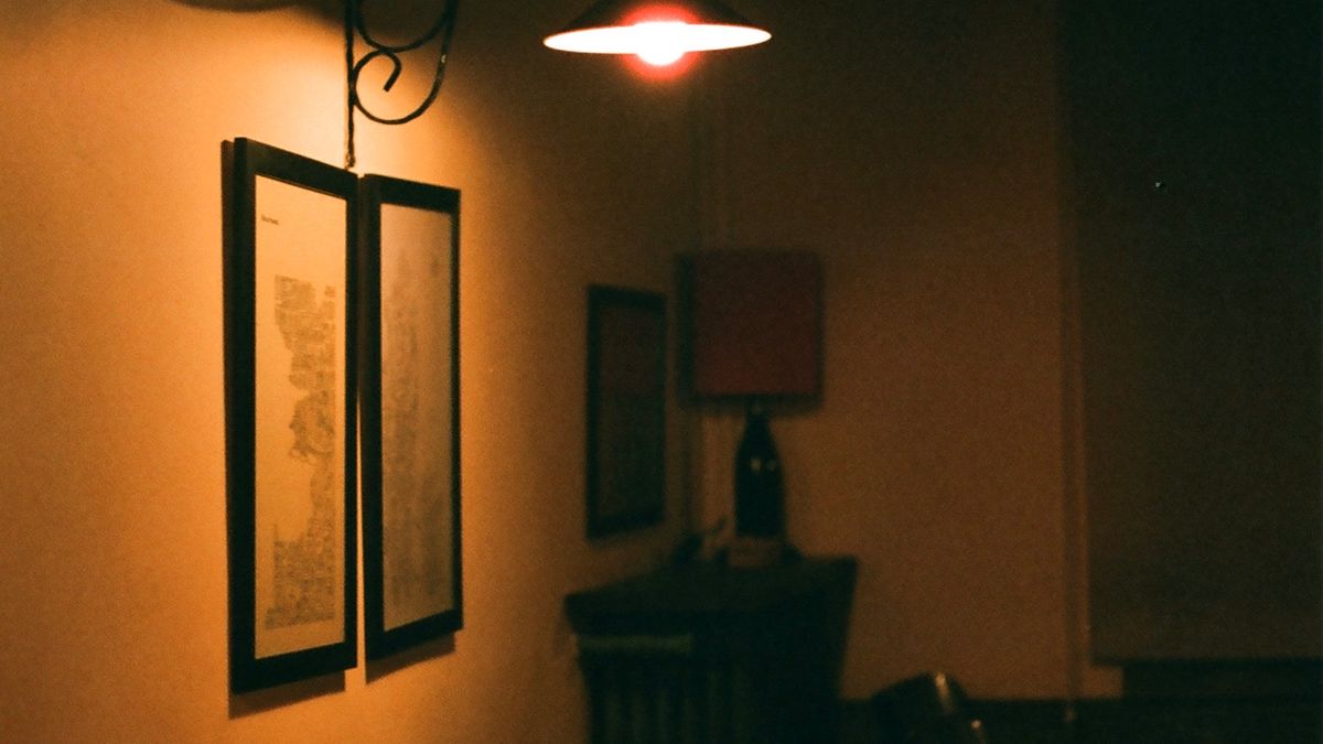 A quiet room lit by one warm lamp, with framed prints on a plain wall