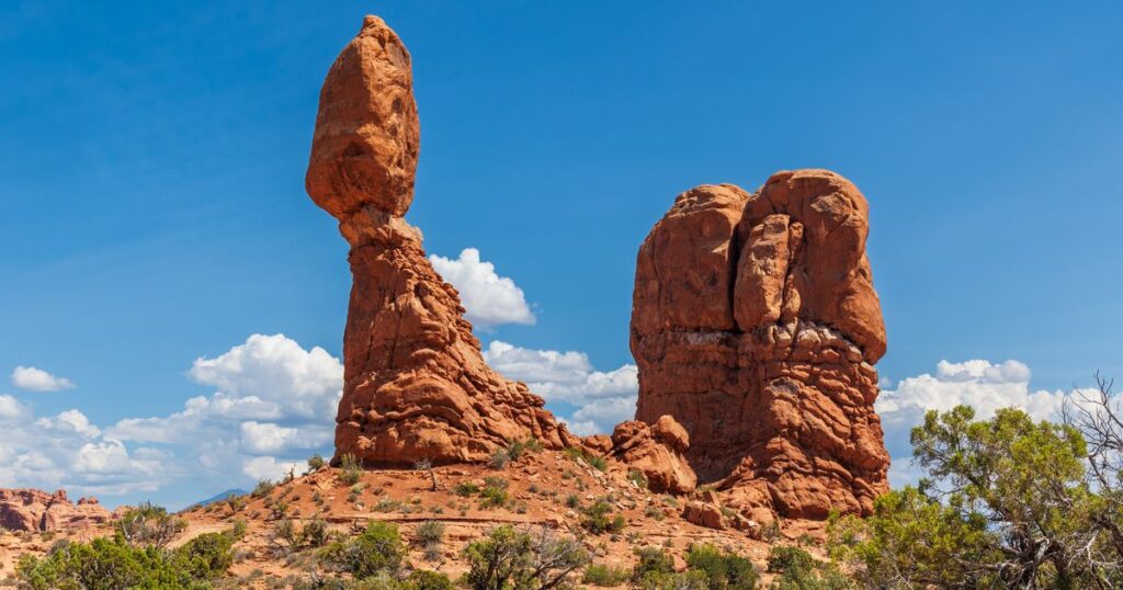 Two red rock formations standing apart on a desert ridge under a clear sky