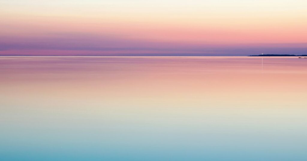A completely still sea at dusk, pink and pale blue, with an unbroken horizon