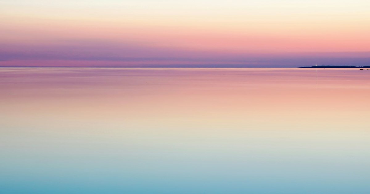 A completely still sea at dusk, pink and pale blue, with an unbroken horizon