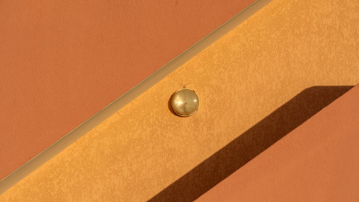 A warm ochre wall in low sunlight with a small round lamp and a hard diagonal shadow