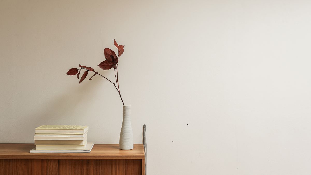A wooden sideboard with a small stack of books and a plain vase