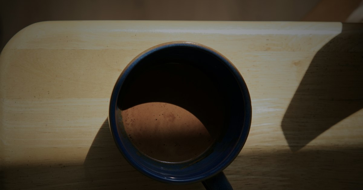 A blue ceramic mug on a pale wooden surface with morning light across it