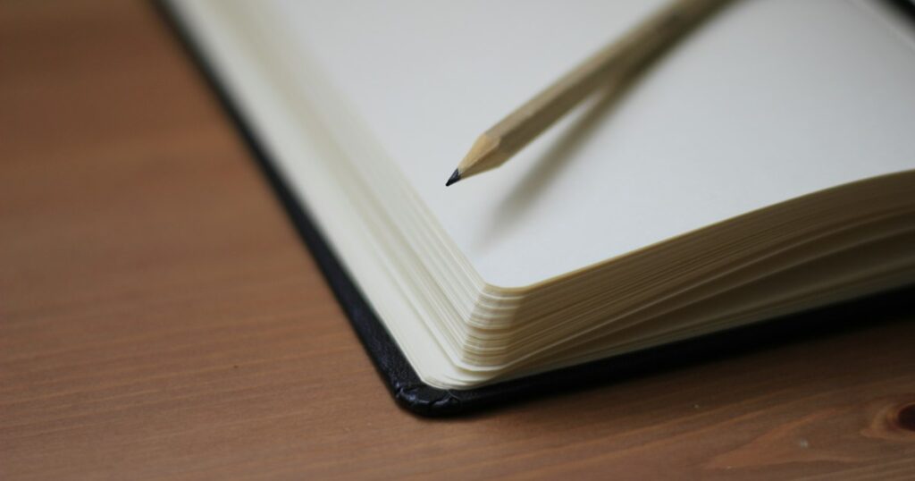 An open notebook with blank pages and a pencil resting on a wooden table