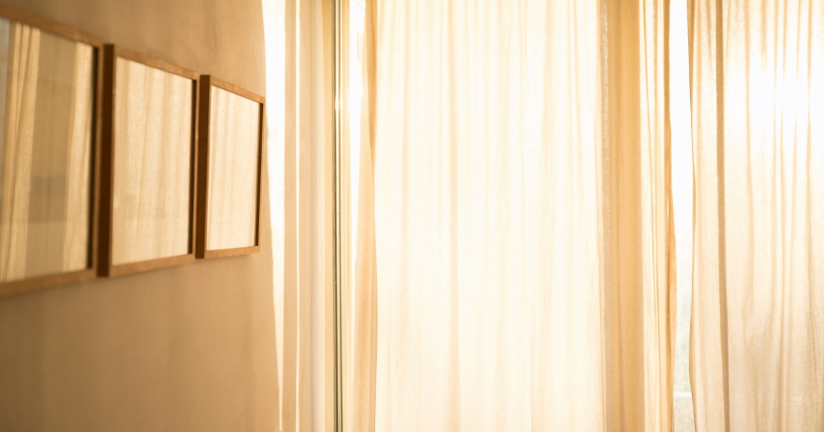 Three empty wooden frames on a pale wall beside a sunlit curtain