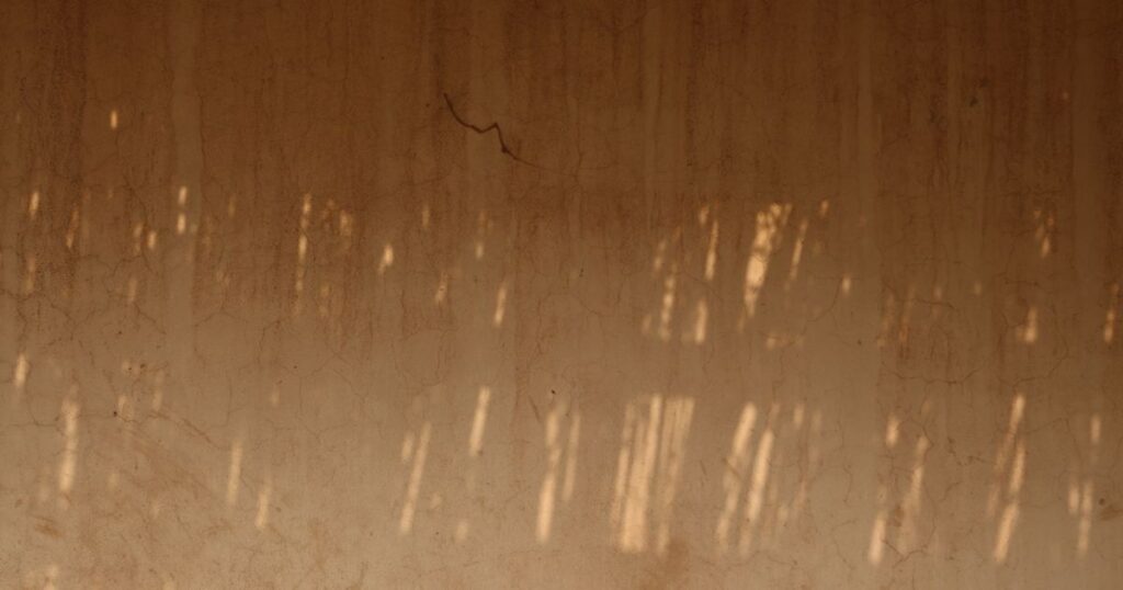 A warm ochre plaster wall in dappled light with one fine crack running through it
