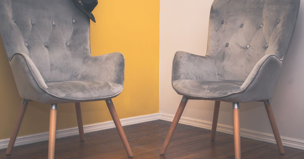 Two grey velvet armchairs standing apart in the corner of a room with a warm yellow wall and a wooden floor