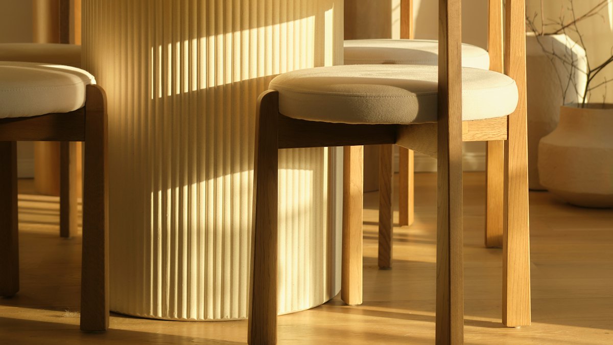 Two empty wooden chairs with pale cushions beside a table in low afternoon light