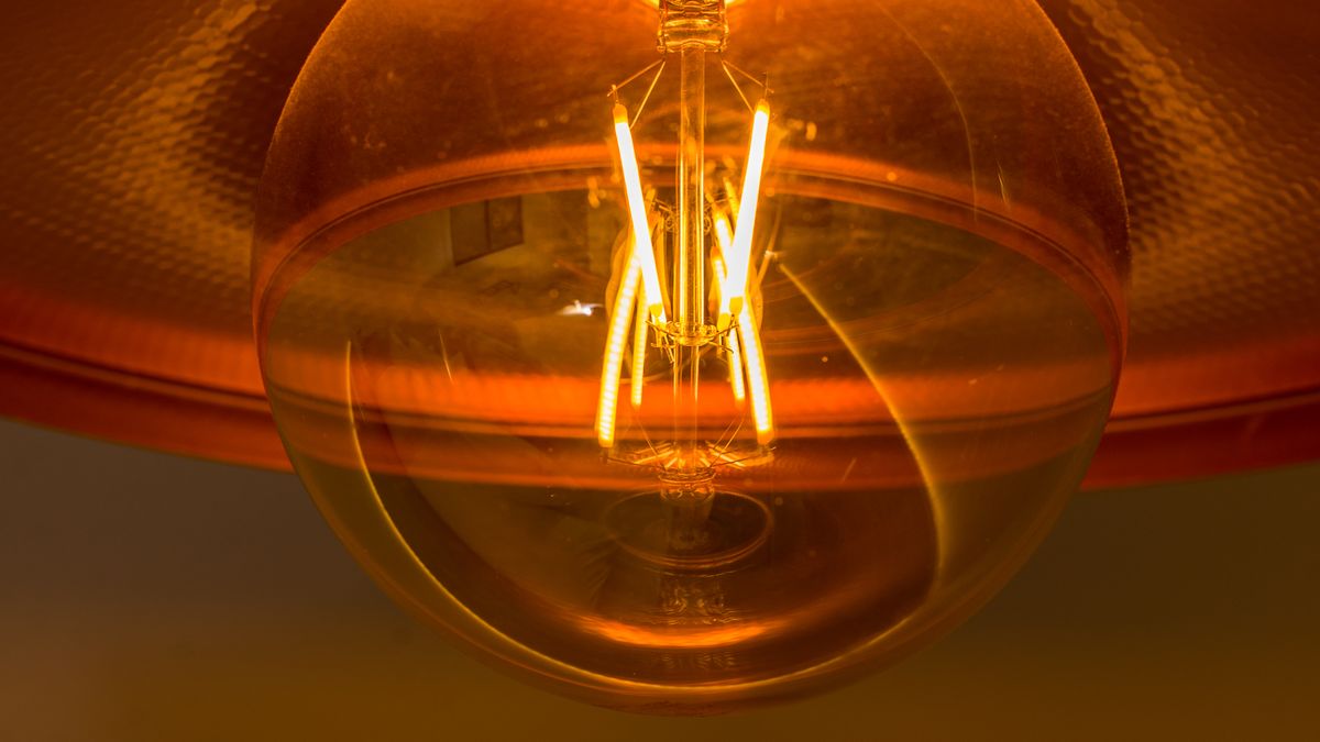 A glowing filament bulb seen close up under an amber shade