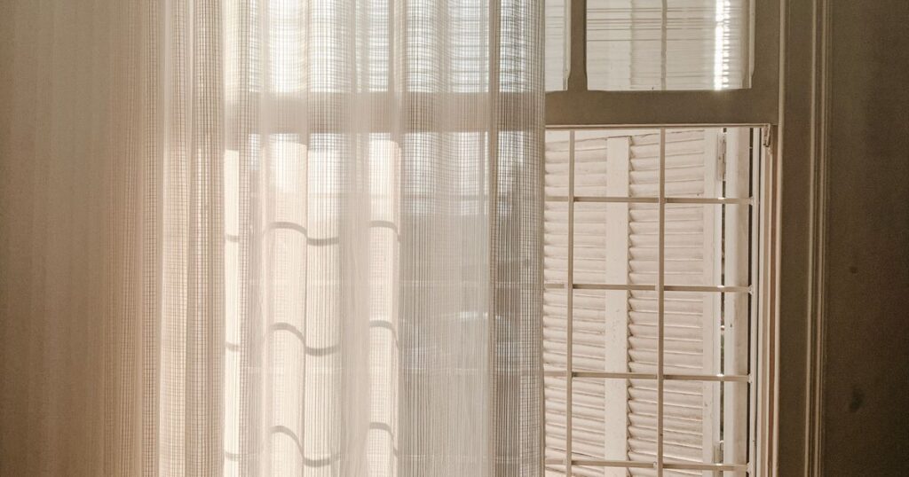 Late afternoon light coming through a sheer curtain beside an open shuttered window