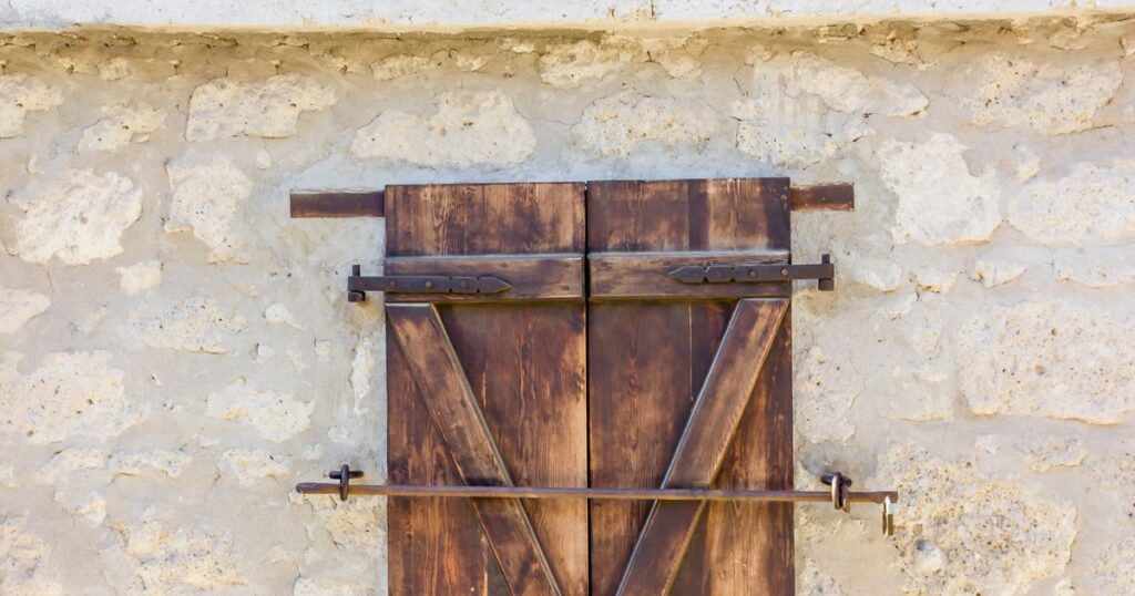 A closed wooden shutter set into a pale stone wall