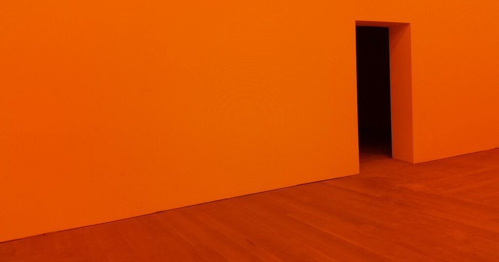 An orange room with an open doorway leading into a dark space.