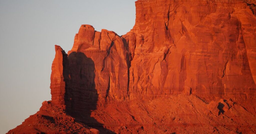 A great red rock wall lit by late sun, with one buttress standing in shadow