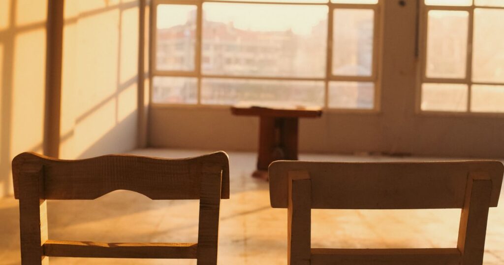 Two wooden chairs facing a bright window in an empty room at golden hour