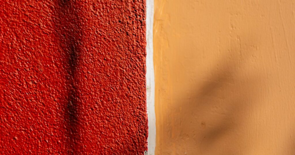 A rough red wall meeting a smooth ochre wall, divided by a thin pale line