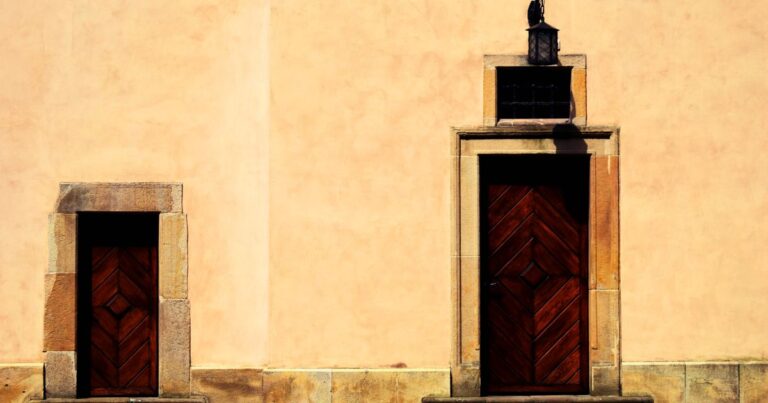 Two closed wooden doors set in a warm ochre wall in sunlight