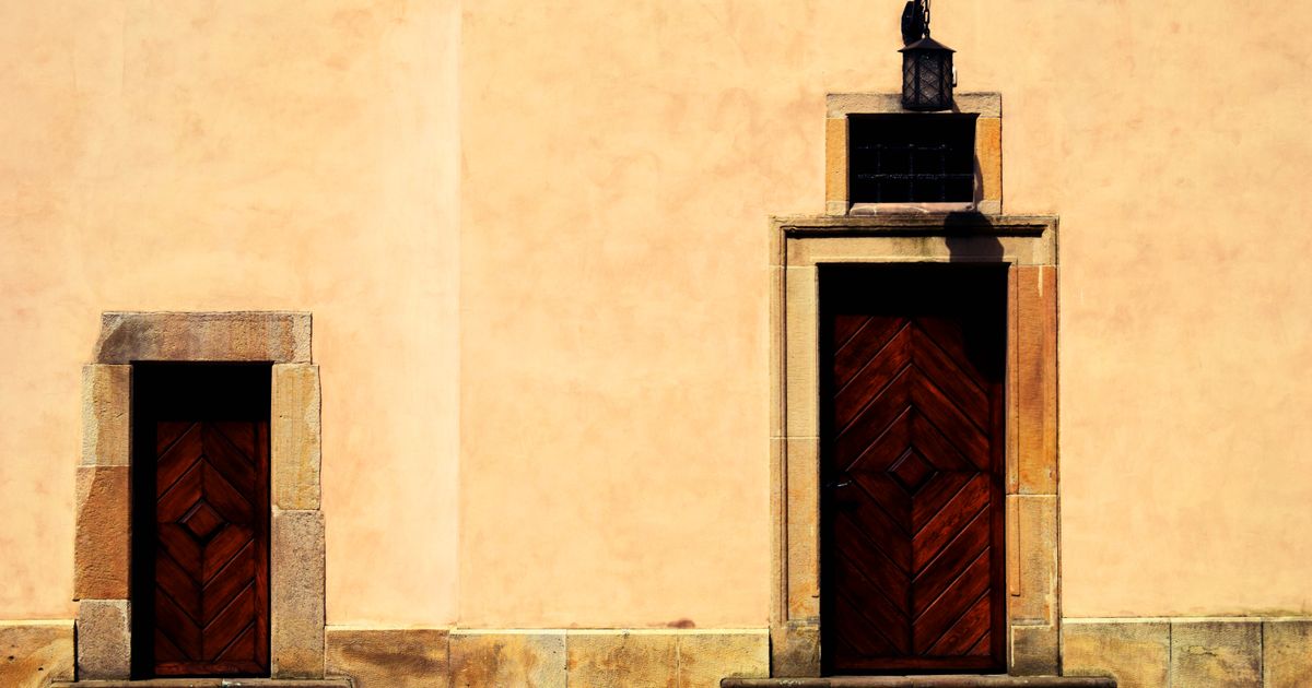 Two closed wooden doors set in a warm ochre wall in sunlight