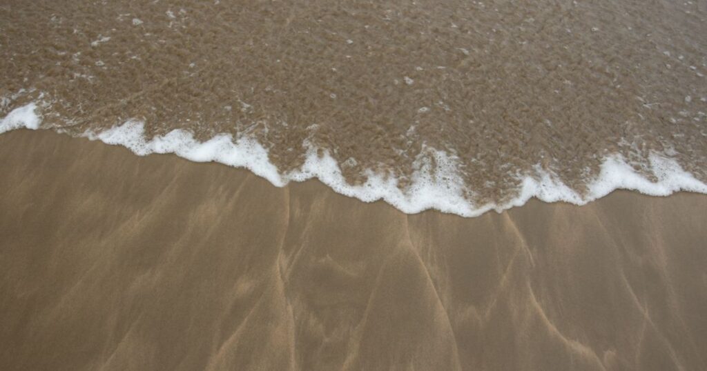 The edge of a wave meeting wet sand on an empty beach